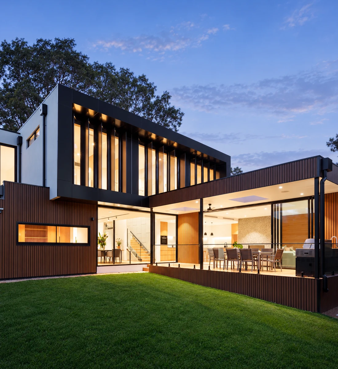 Modern two-story home with warmly lit windows and an open lawn at dusk